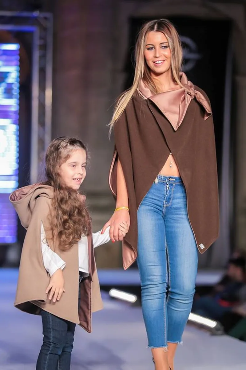 Mãe e filha em capas em tons de camel e bege, de mãos dadas