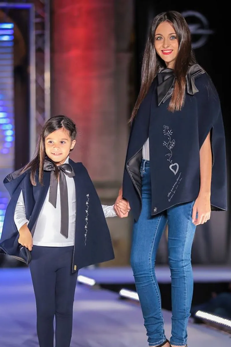 Mãe e filha em capas azul-marinho a condizer, uma com laço ao pescoço